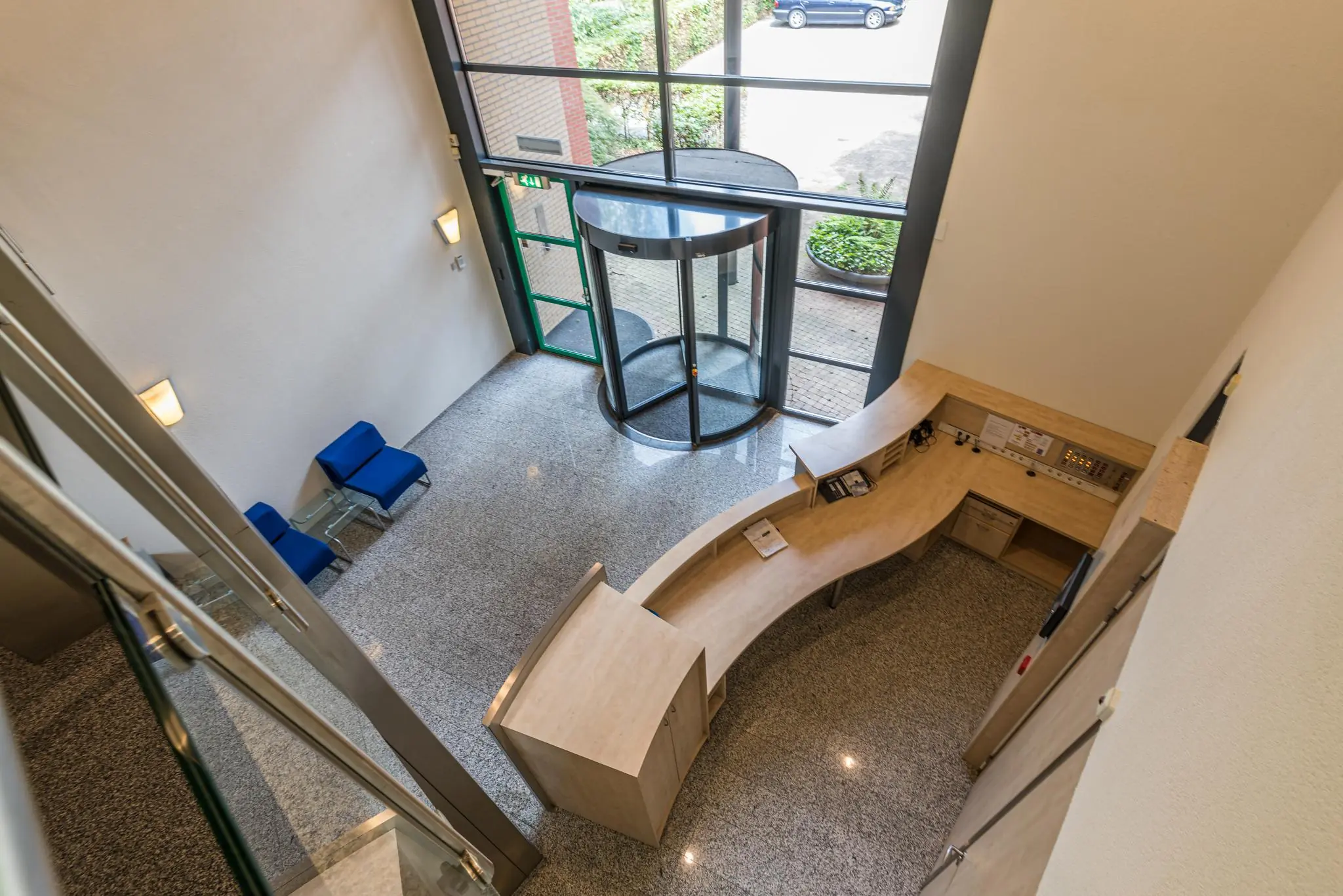 Inkomhal aan de Laan Blussé van Oud-Alblas met een houten receptiebalie, glazen draaideur en zitgedeelte met blauwe stoelen.